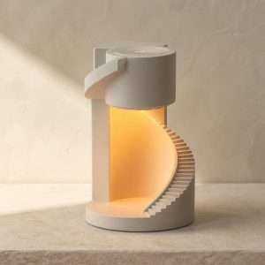 White plaster spiral staircase candle warmer lamp with a warm glow inside, on a stone ledge against a beige wall