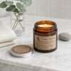 Lit on a marble bathroom counter beside eucalyptus and folded waffle towels, a soy wax jar candle with one wick