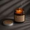 Dark still life: the flame and a thread of smoke above the amber glass of the scented candle jar