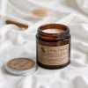 Amber glass jar candle with a kraft label and its silver screw lid off, on white fabric, the GODONLIF amber jar candle