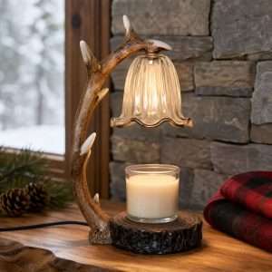 Deer antler lamp lit over a jar candle on a log-slice base, by a stone wall and a snowy window with a plaid throw
