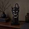 The demon head lamp switched off on a walnut sideboard with a black vase and bare branches