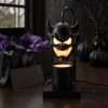 The demon head lamp lit beside a gift box with purple tissue and matte black pumpkins