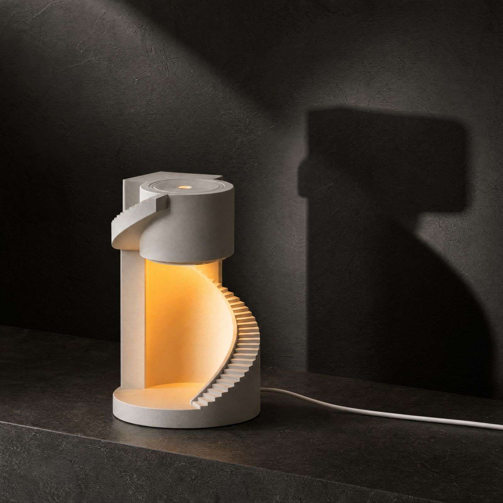 Dark studio shot of the spiral staircase lamp lit against a charcoal wall