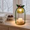 Green bell warmer lit on a snowy windowsill with pine cones and a white throw, emerald green Christmas decor