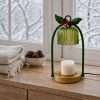 Unlit fluted green glass bell and round gold base on a wood sill, jewel tone decor with a tartan bow