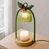 Angled view of the lit green glass candle warmer on a side table, twisted green stems and a gold base