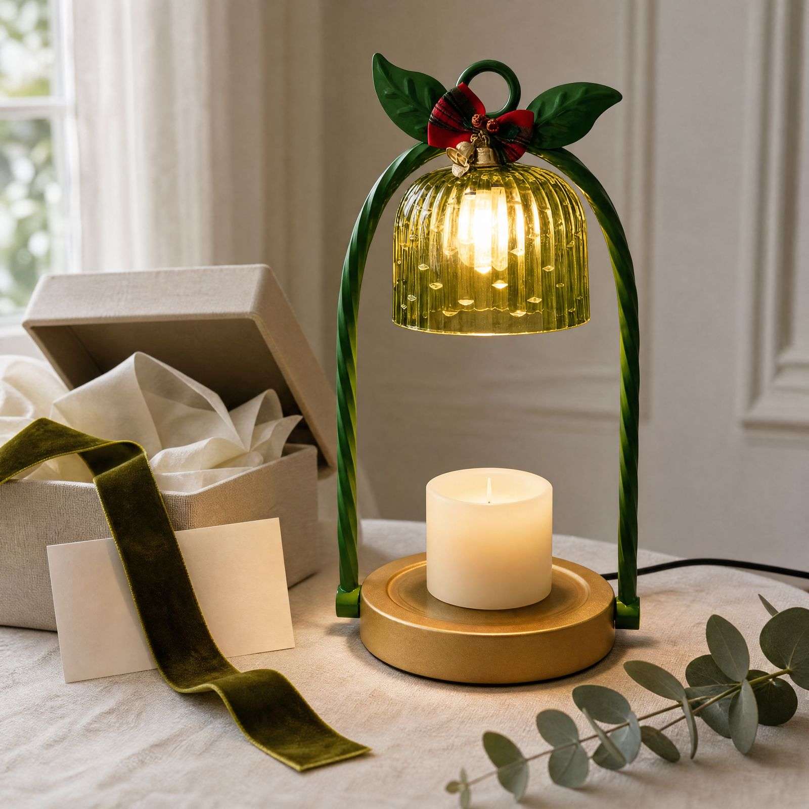 Green candle warmer lamp lit beside an open gift box, velvet ribbon and a blank card on a linen cloth