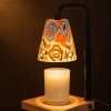 Floral ceramic candle warmer glowing against a dark wall, painted roses and daisies lit from inside