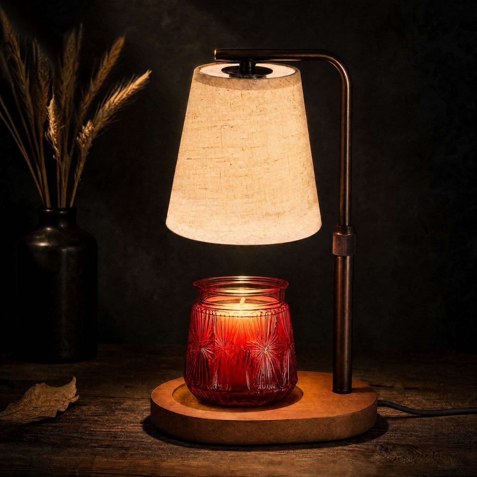Dark still life: warm light through the linen-look shade onto a red jar, dried wheat behind, a rustic candle warmer