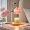 Pink glass lily of the valley lamp lit over a jar candle on a wood base, on a pink marble nightstand beside peonies