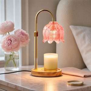 Pink glass lily of the valley lamp lit over a jar candle on a wood base, on a pink marble nightstand beside peonies