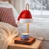 Red Santa hat candle warmer lamp on a gold pole, lit above a blue holiday candle tin on a square dark wood base