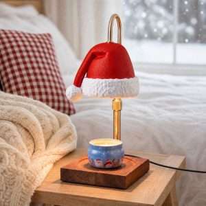 Red Santa hat candle warmer lamp on a gold pole, lit above a blue holiday candle tin on a square dark wood base