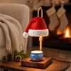 Santa hat warmer lit on a side table with pinecones and a pine sprig, stockings by the fire behind it, a holiday wax warmer