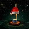 Close-up of the lit Santa hat shade on green velvet with falling snow, blue candle tin below the white fur brim