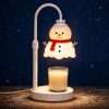 Lit snowman warmer and its glass jar candle in falling snow on a snow-dusted wooden plank, snowman candle warmer detail